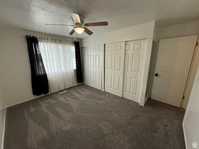 unfurnished bedroom featuring a closet, ceiling fan, dark colored carpet, and a textured ceiling