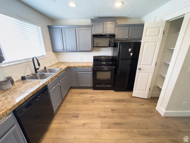 kitchen featuring light wood-style flooring, a sink, black appliances, and gray cabinets