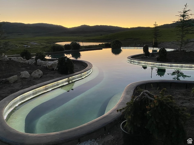 pool at dusk featuring a water and mountain view