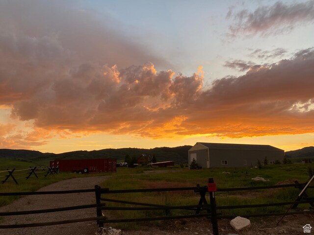 yard at dusk with a mountain view, a rural view, an outbuilding, a pole building, and fence