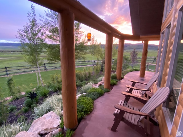patio terrace at dusk featuring a rural view, a yard, and fence