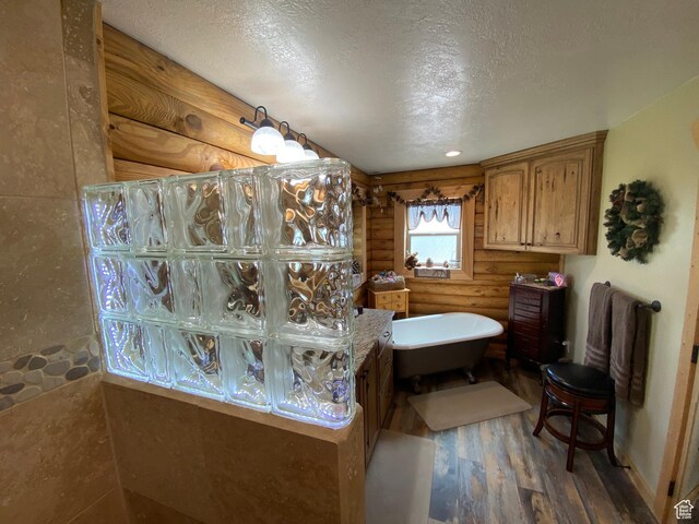 full bathroom with rustic walls, wood finished floors, a freestanding bath, and a textured ceiling