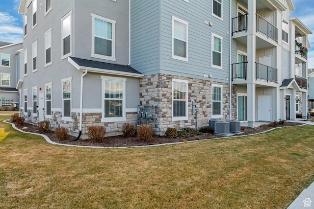 exterior space featuring a yard, stucco siding, stone siding, and central AC