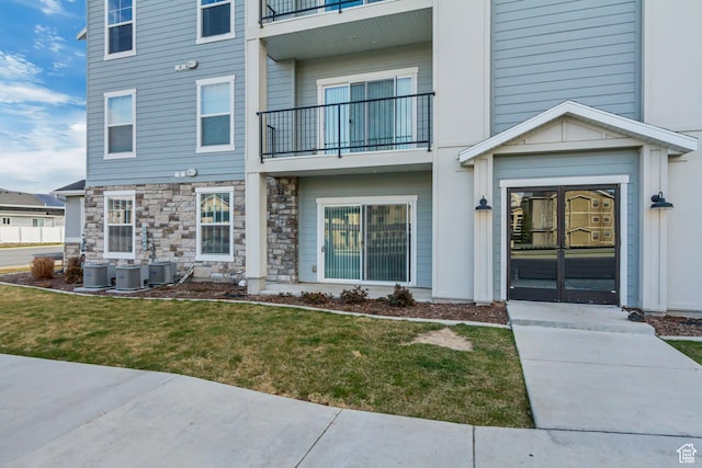 doorway to property with central AC, stone siding, and a lawn