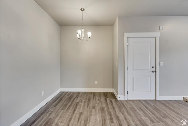 unfurnished dining area with baseboards, an inviting chandelier, and wood finished floors