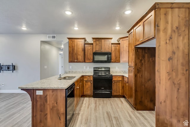 kitchen with a sink, light wood-type flooring, a peninsula, brown cabinetry, and black appliances