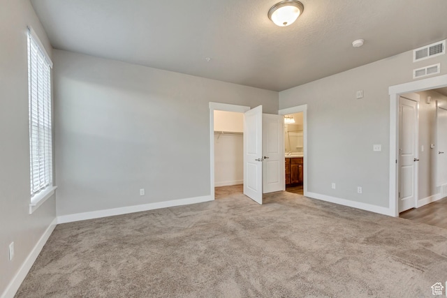 unfurnished bedroom featuring visible vents, baseboards, a walk in closet, and carpet