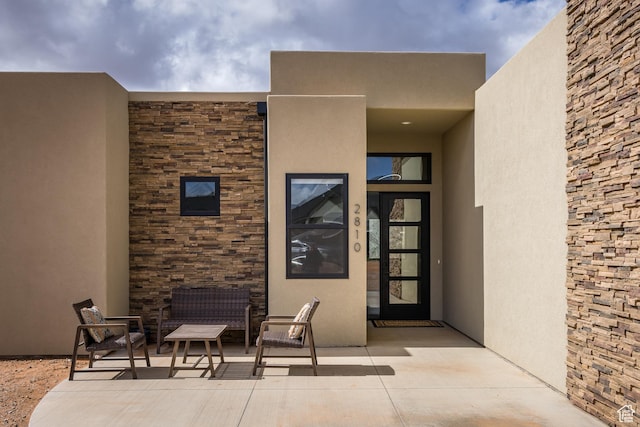 doorway to property featuring stone siding, a patio, and stucco siding