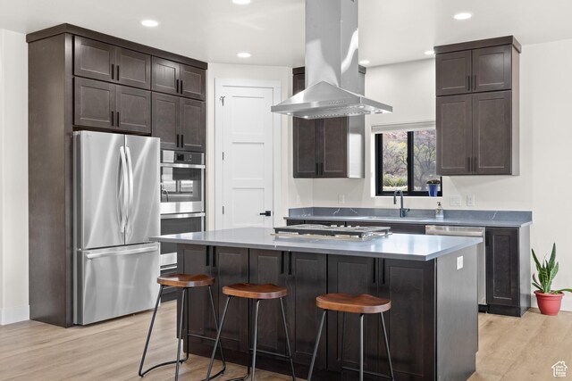 kitchen with stainless steel appliances, dark brown cabinetry, light wood-style floors, and island exhaust hood