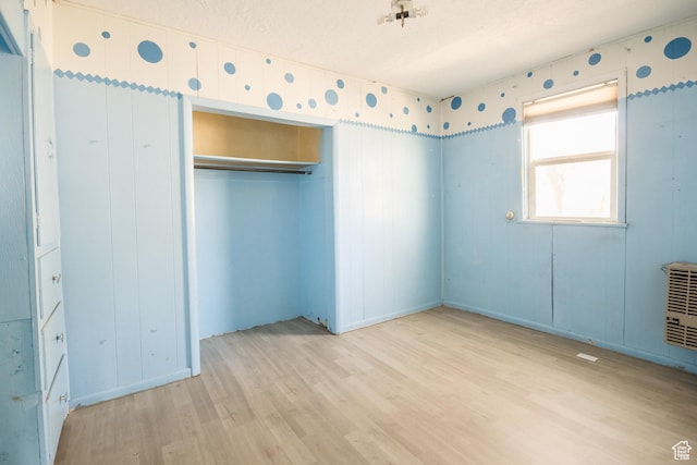 unfurnished bedroom with wood finished floors, a closet, and heating unit
