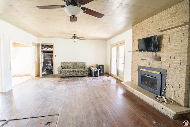 living area with a stone fireplace, a ceiling fan, and wood finished floors
