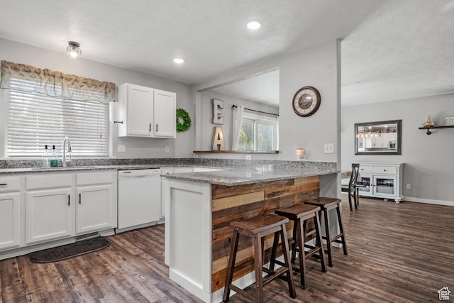 kitchen with dishwasher, a sink, a kitchen bar, white cabinetry, and dark wood-type flooring
