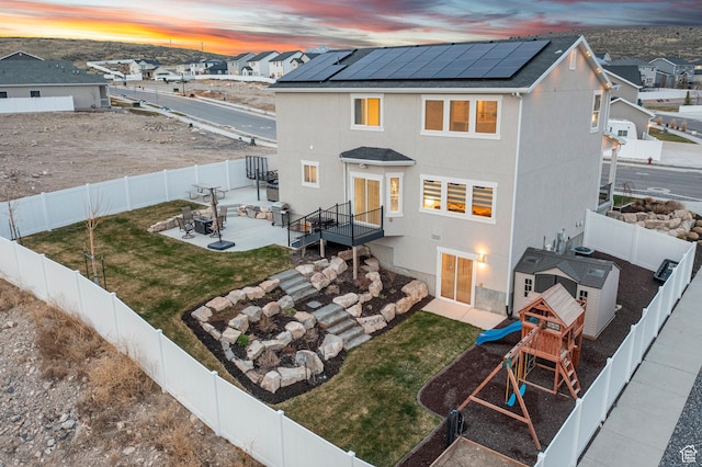 7091 N Oquirrh Ranch Pkwy, Eagle Mountain, UT 84005 - back of property at dusk with a lawn, a fenced backyard, a patio area, and solar panels