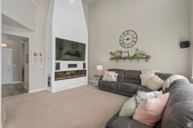 7091 N Oquirrh Ranch Pkwy, Eagle Mountain, UT 84005 - living room featuring a glass covered fireplace, a towering ceiling, baseboards, and carpet floors