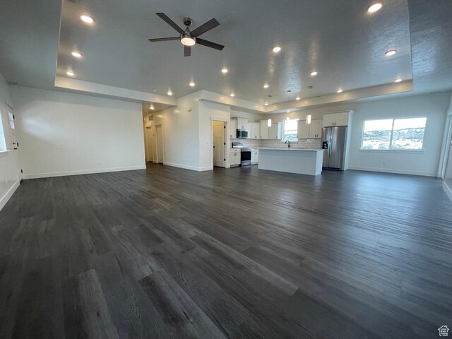 631 N 4250 W, Vernal, UT 84078 - unfurnished living room with a tray ceiling, dark wood-style flooring, baseboards, and a ceiling fan