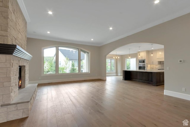 15724 S Rolling Bluff Dr, Draper Ut Cnty, UT 84020 - unfurnished living room with crown molding, baseboards, light wood-style floors, a large fireplace, and a chandelier
