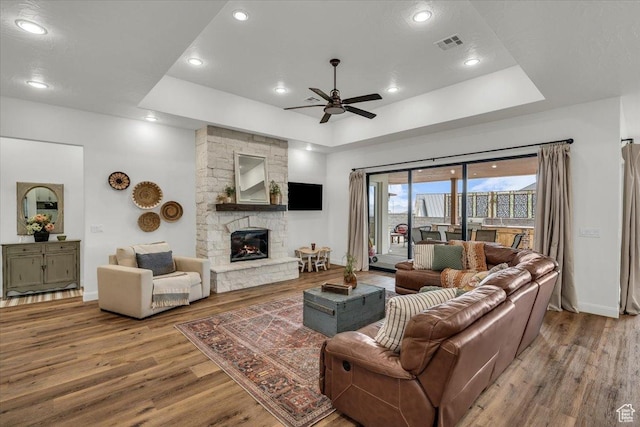 living room featuring a fireplace, visible vents, a tray ceiling, ceiling fan, and wood finished floors