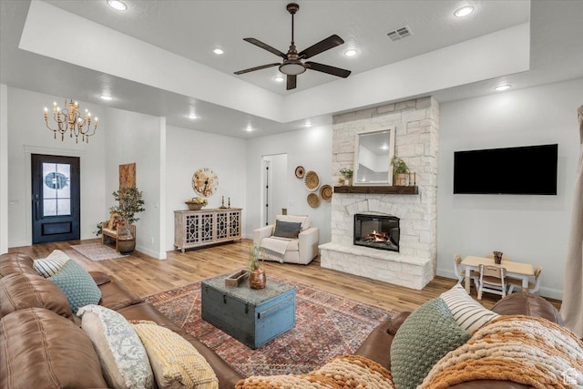 living room featuring ceiling fan with notable chandelier, wood finished floors, a stone fireplace, and recessed lighting