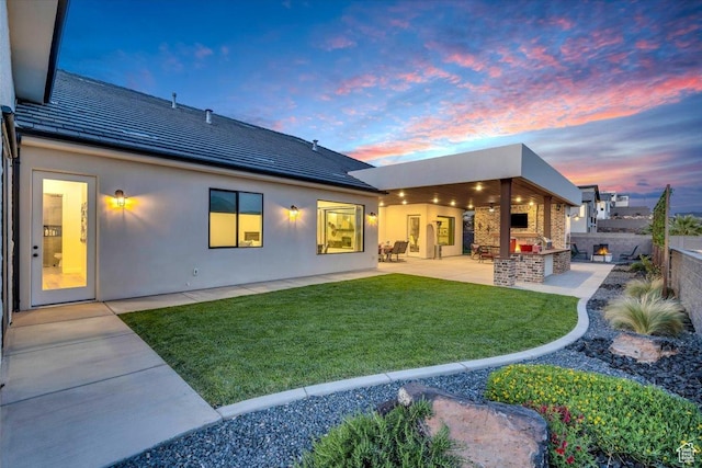 back of property at dusk featuring a patio, stucco siding, fence, and a lawn
