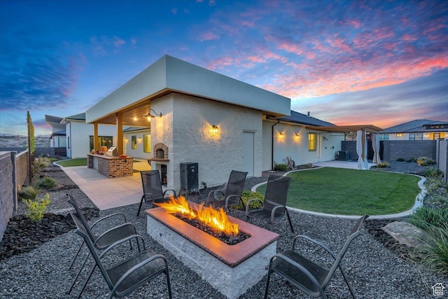 rear view of property with a fire pit, a patio area, a lawn, a fenced backyard, and an outdoor kitchen