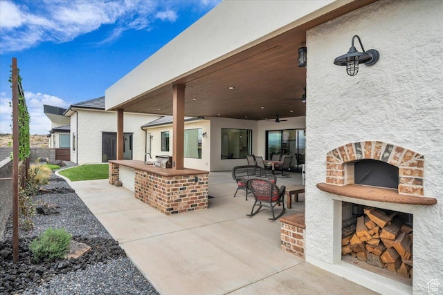 view of patio featuring exterior kitchen, ceiling fan, fence, and exterior fireplace