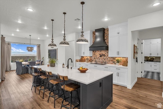 kitchen with custom range hood, light wood-type flooring, a sink, and backsplash