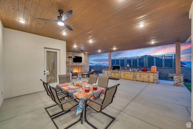 view of patio / terrace with an outdoor brick fireplace, outdoor dining space, fence, and a ceiling fan