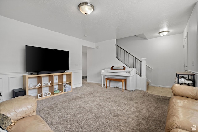 carpeted living room with a wainscoted wall, a textured ceiling, and stairs