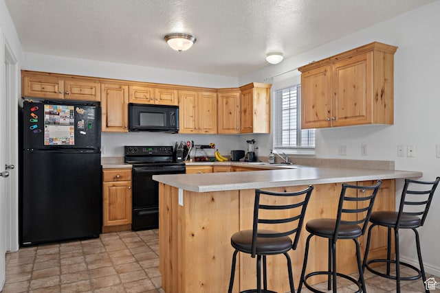 kitchen featuring a peninsula, black appliances, a breakfast bar, a sink, and light countertops