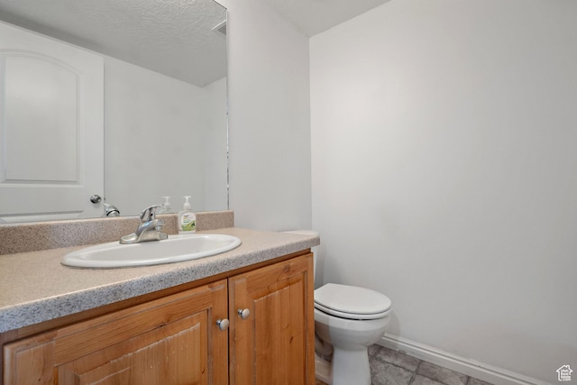 half bath featuring baseboards, toilet, a textured ceiling, vanity, and tile patterned floors