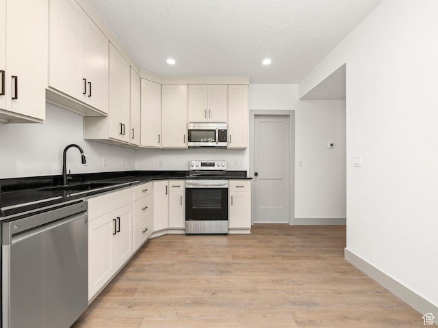 kitchen featuring a sink, dark countertops, recessed lighting, stainless steel appliances, and light wood-style flooring