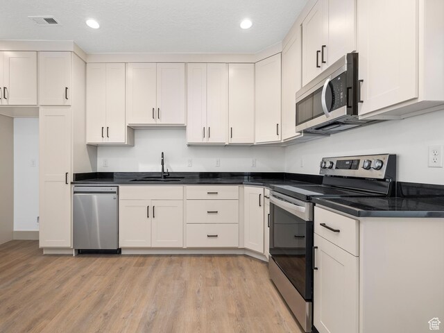 kitchen with visible vents, a sink, appliances with stainless steel finishes, white cabinetry, and light wood finished floors