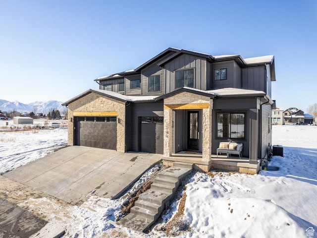 view of front of property featuring driveway, board and batten siding, stone siding, and an attached garage