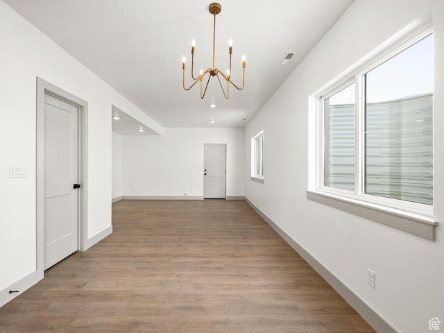 spare room with visible vents, baseboards, light wood-type flooring, and an inviting chandelier