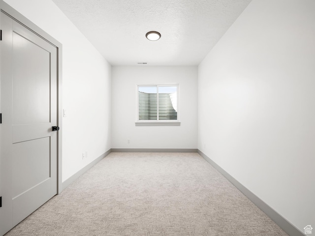 spare room featuring visible vents, baseboards, light colored carpet, and a textured ceiling