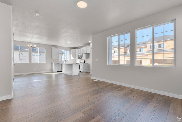 6633 N Price, Eagle Mountain, UT 84005 - unfurnished living room featuring a chandelier, light wood-style flooring, baseboards, and a textured ceiling