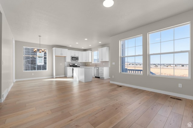6658 W Spring Snow Ln, Herriman, UT 84096 - unfurnished living room with a notable chandelier, light wood-type flooring, baseboards, recessed lighting, and visible vents