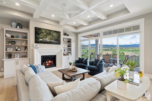 living area featuring a glass covered fireplace, coffered ceiling, recessed lighting, and light wood-style flooring