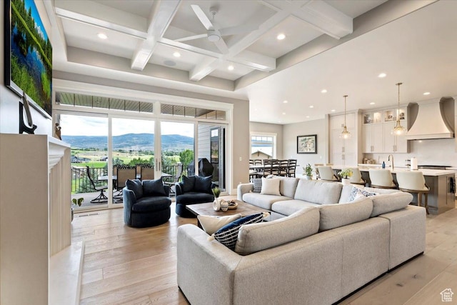 living area featuring light wood-style floors, coffered ceiling, ceiling fan, and beamed ceiling