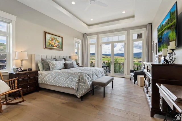 bedroom featuring access to outside, recessed lighting, light wood-style flooring, and a tray ceiling