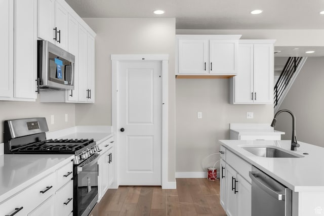 kitchen with light countertops, white cabinetry, stainless steel appliances, a sink, and wood finished floors