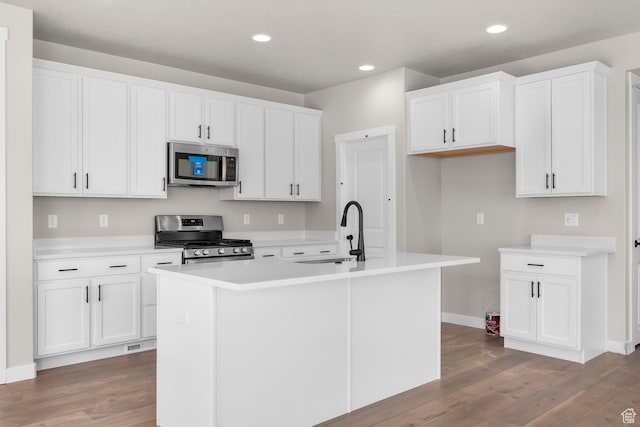 kitchen with a sink, an island with sink, white cabinetry, wood finished floors, and stainless steel appliances
