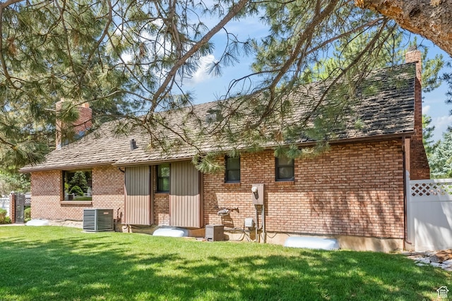 rear view of house with central AC, a yard, a chimney, fence, and brick siding