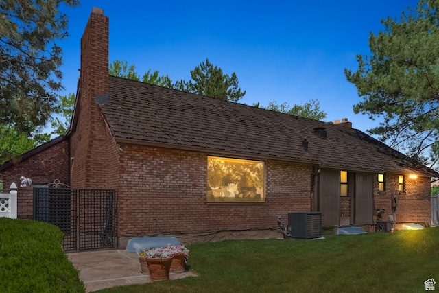rear view of property featuring central air condition unit, a chimney, a lawn, and brick siding