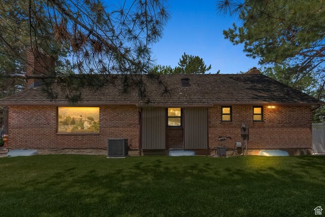 back of house featuring brick siding, a lawn, and central air condition unit