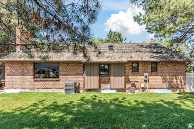 back of property featuring brick siding, cooling unit, a lawn, and a chimney