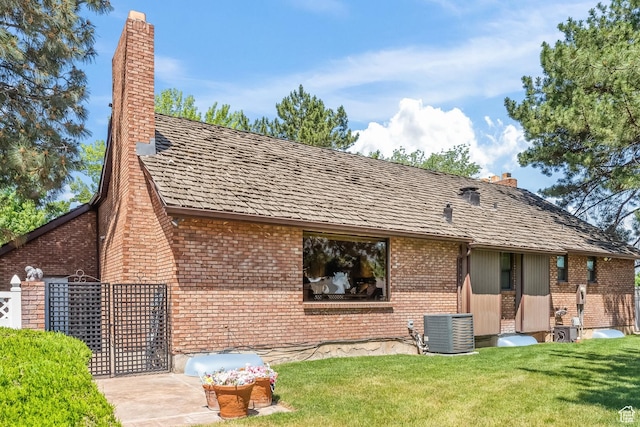 back of house featuring brick siding, cooling unit, a lawn, and a chimney
