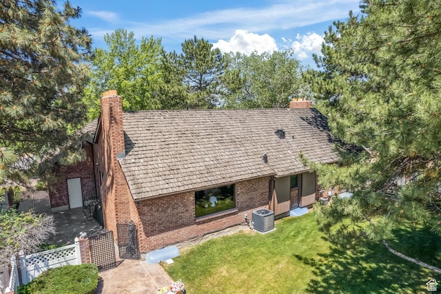 back of property with brick siding, central air condition unit, a chimney, and a lawn
