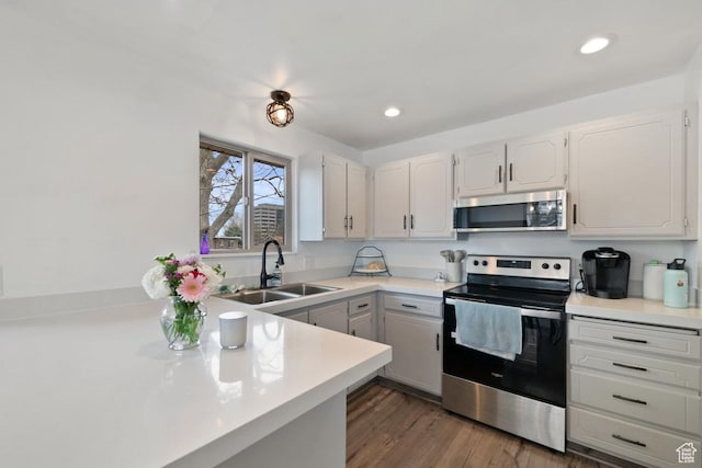 kitchen featuring white cabinets, a sink, light countertops, appliances with stainless steel finishes, and dark wood-style floors