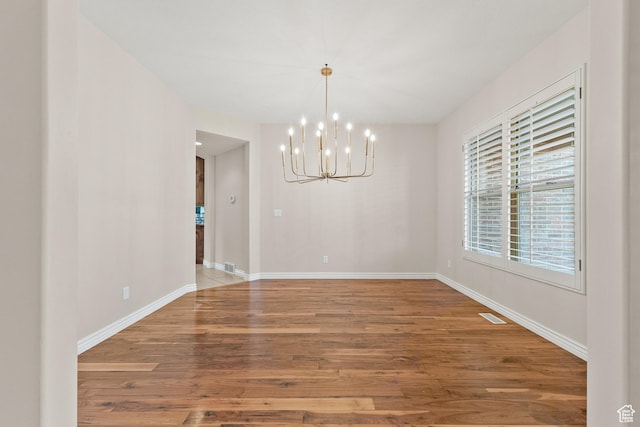 unfurnished dining area with visible vents, baseboards, an inviting chandelier, and wood finished floors